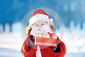 Funny little boy wearing Santa Claus costume in winter snowy park