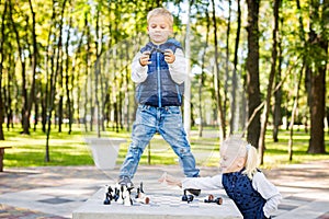 Funny little brother and sister of Caucasian ethnicity play on a public chess venue in a city park. Children frolic and indulge
