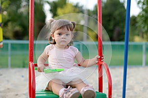 Funny little child, adorable preschooler girl in pretty dress having fun on a swin