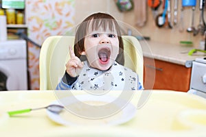 Funny little child eating wheat porridge with pumpkin