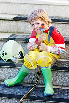 Funny little child of four years having fun as fireman, in uniform and helmet.