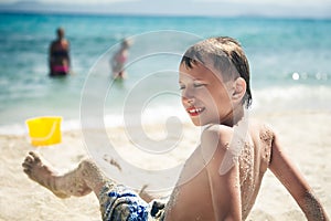 Funny little child sitting on sandy beach smiling