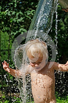 Funny little child  splashing with cold water. Water games on hot day in backyard. Hardening for health. Strengthen your body.