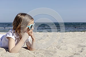 Funny little girl 7 years old in sunglasses lies on the beach