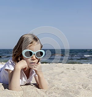 Funny little girl 7 years old in sunglasses lies on the beach