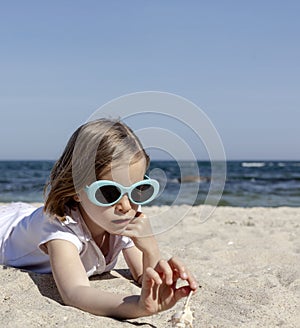 Funny little girl 7 years old in sunglasses lies on the beach