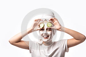 Funny little girl applying facial mask, holding cucumber slices. Teen girl taking care of her skin, cleaning the pores. Face mask