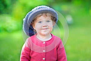 Funny little girl in big knitted hat in the garden