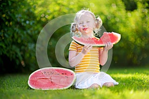 Funny little girl biting a slice of watermelon outdoors