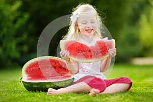 Funny little girl biting a slice of watermelon outdoors on warm and sunny summer day