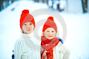 Funny little girl and boy in a red knitted hat and scarf and white pullover playing outside in winter time. Kids play outdoors in