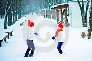 Funny little girl and boy in a red knitted hat and scarf and white pullover playing outside in winter time. Kids play outdoors in