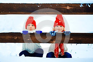 Funny little girl and boy in a red knitted hat and scarf and white pullover playing outside in winter time. Kids play outdoors in