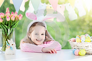 Funny little girl in bunny ears at breakfast on Easter morning at table with Easter eggs