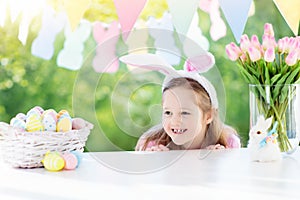 Funny little girl in bunny ears at breakfast on Easter morning at table with Easter eggs