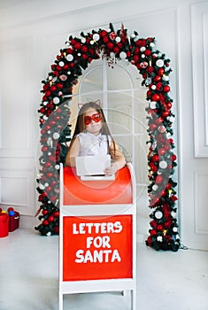 Funny little girl with cat`s ears stands near mailbox indoors