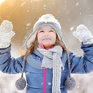 Funny little girl catching snowflakes in winter park