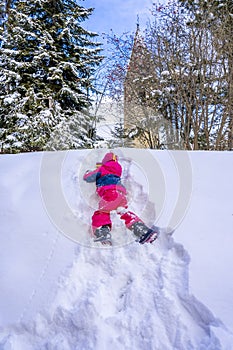 Funny little girl in colorful winter suit climbs the snow hill. Kids play and jump in snowy forest. Child playing with