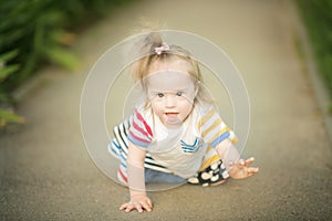 Funny little girl with Down syndrome creeps along the path
