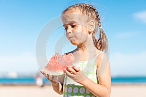 Funny little girl eat watermelon sunny summer day at ocean beach. Cute caucasian female child enjoy summer fruit bite slice of