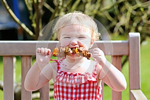 Funny little girl eating grilled meat from spoon