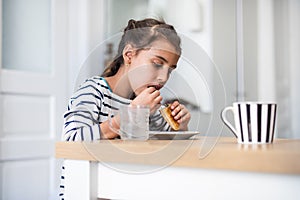 Funny little girl eating handmade cookie and looking at camera. Beautiful smart child holding a freshly baked biscuit. Little girl