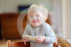 Funny little girl eating sandwich at home