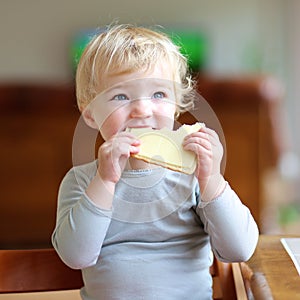 Funny little girl eating sandwich at home