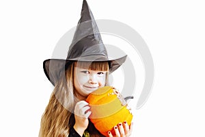 Funny Little Girl In A Halloween Witch Costume With A Pumpkin. A child in a black hat is getting ready for Halloween at home.