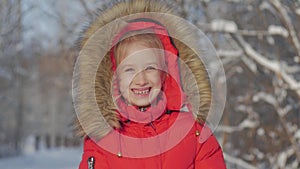 Funny little girl having fun in beautiful winter park. Winter portrait of adorable small girl looks into the camera.