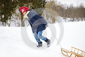 Funny little girl having fun with a sleigh in beautiful winter park. Cute child playing in a snow.