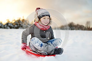 Funny little girl having fun with a sleigh in beautiful winter park. Cute child playing in a snow