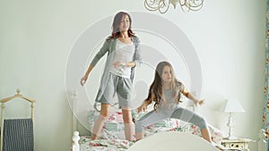 Funny little girl with her loving mother have fun dancing modern style together jumping on bed during morning at home