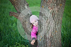 Funny little girl hides behind tree