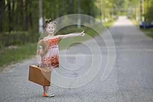 Funny little girl hitchhiker with a suitcase and a teddy bear. Travel.