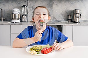 Funny little girl holding tomato and cheese fork in her mouth. A young girl is having breakfast in the kitchen. Selected