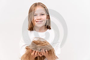 funny little girl holds in hands cropped hair after cutting on white background.