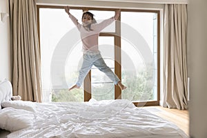 Funny little girl jumping on bed in modern bedroom