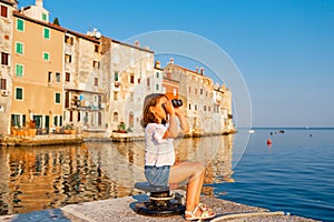 Funny little girl looking through vintage binoculars on sunny summer day. Rovinj town in background. Travel and adventure concept