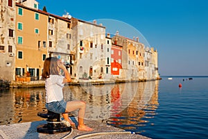 Funny little girl looking through vintage binoculars on sunny summer day. Rovinj town in background. Travel and adventure concept