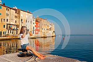 Funny little girl looking through vintage binoculars on sunny summer day. Rovinj town in background. Travel and adventure concept