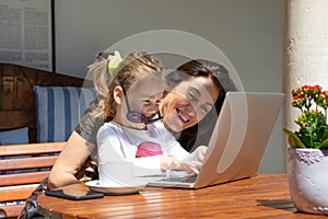 Funny little girl and mother laughing typing on laptop