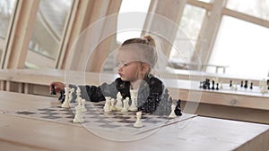 Funny little girl playing chess with chess pieces in a club