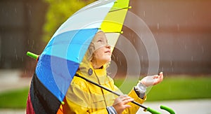 Funny little girl playing in the garden under the autumn rain. Kid wearing yellow waterproof coat and boots holding