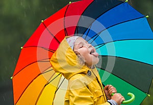 Funny little girl playing in the garden under the autumn rain. Kid wearing yellow waterproof coat and boots holding