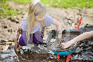 Funny little girl playing in a large wet mud puddle on sunny summer day. Child getting dirty while digging in muddy soil.