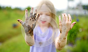 Funny little girl playing in a large wet mud puddle on sunny summer day. Child getting dirty while digging in muddy soil