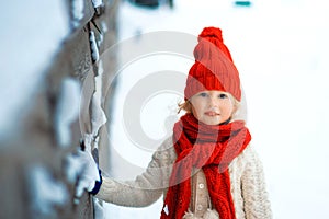 Funny little girl in a red knitted hat and scarf and white pullover playing outside in winter time. Kids play outdoors in winter.