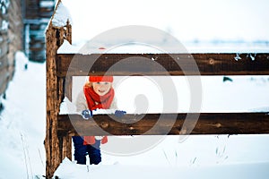 Funny little girl in a red knitted hat and scarf and white pullover playing outside in winter time. Kids play outdoors in winter.