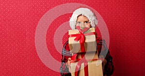 Funny little girl in santa hat, fall Christmas gift boxes arise in hand isolated on red background,